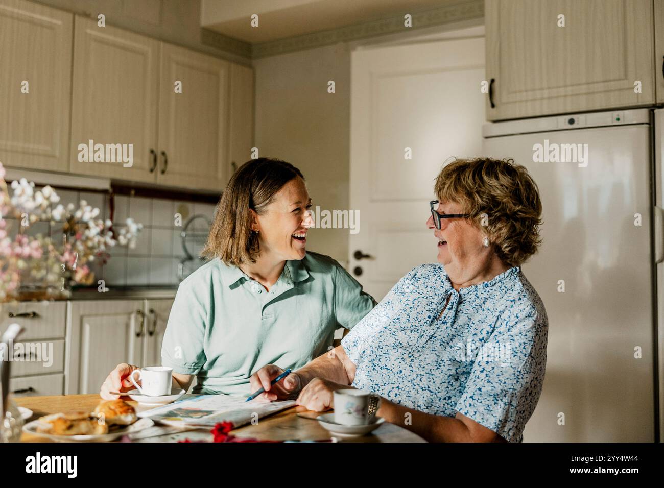 Heureuse infirmière féminine et femme senior passant du temps de loisirs à résoudre le puzzle de mots croisés à la maison Banque D'Images