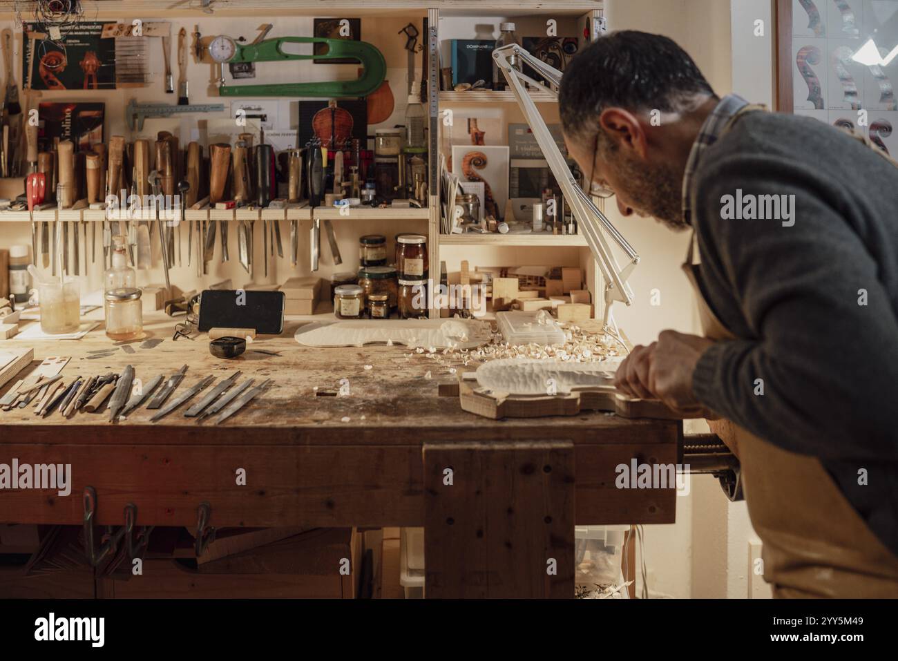 Luthier sur un établi bien équipé, entouré d'outils, travaillant sur une pièce de violon à Crémone, Italie, Europe Banque D'Images