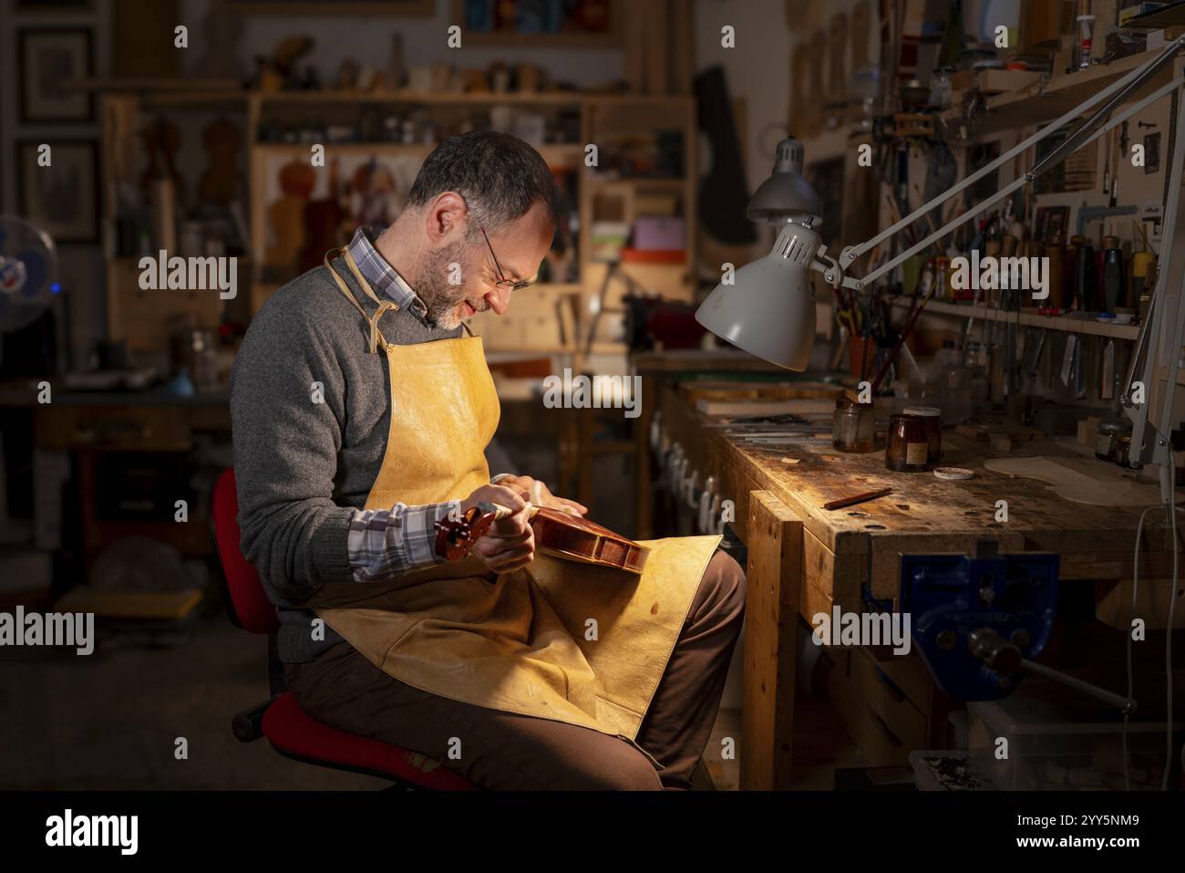 Luthier finissant un violon sous éclairage contrôlé, entouré d'outils de travail du bois à Crémone, Italie, Europe Banque D'Images