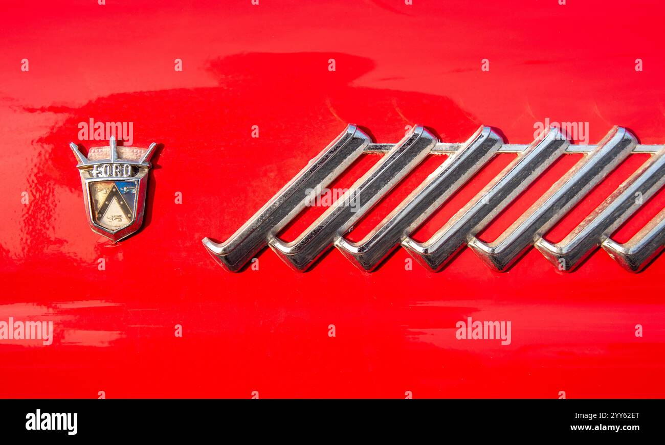 Vue rapprochée d'un logo ford et d'une garniture décorative sur une voiture rouge classique, mettant en valeur le design automobile Banque D'Images