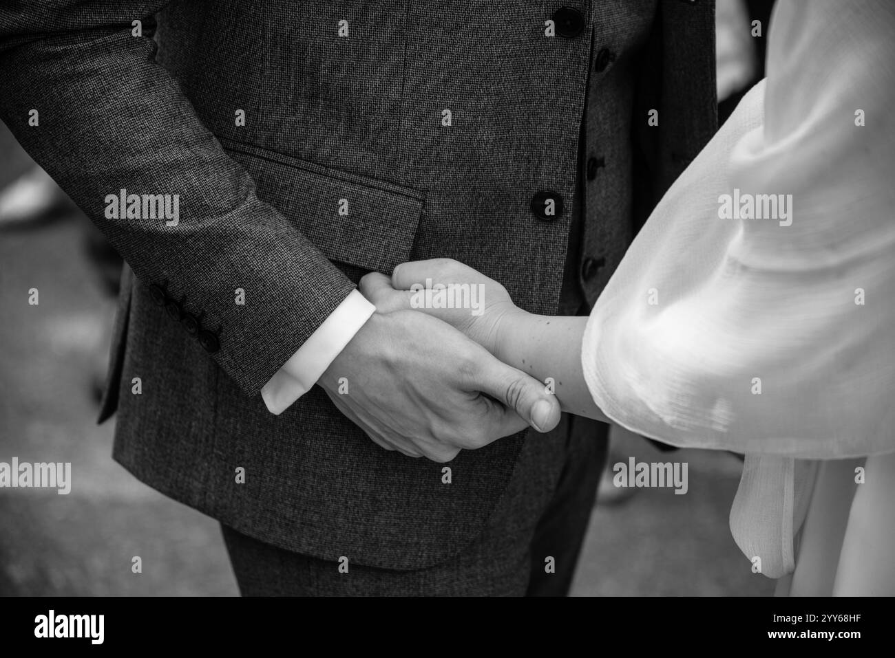 Gros plan photo noir et blanc de mariée et marié tenant leurs mains doucement, élégamment habillé. Banque D'Images