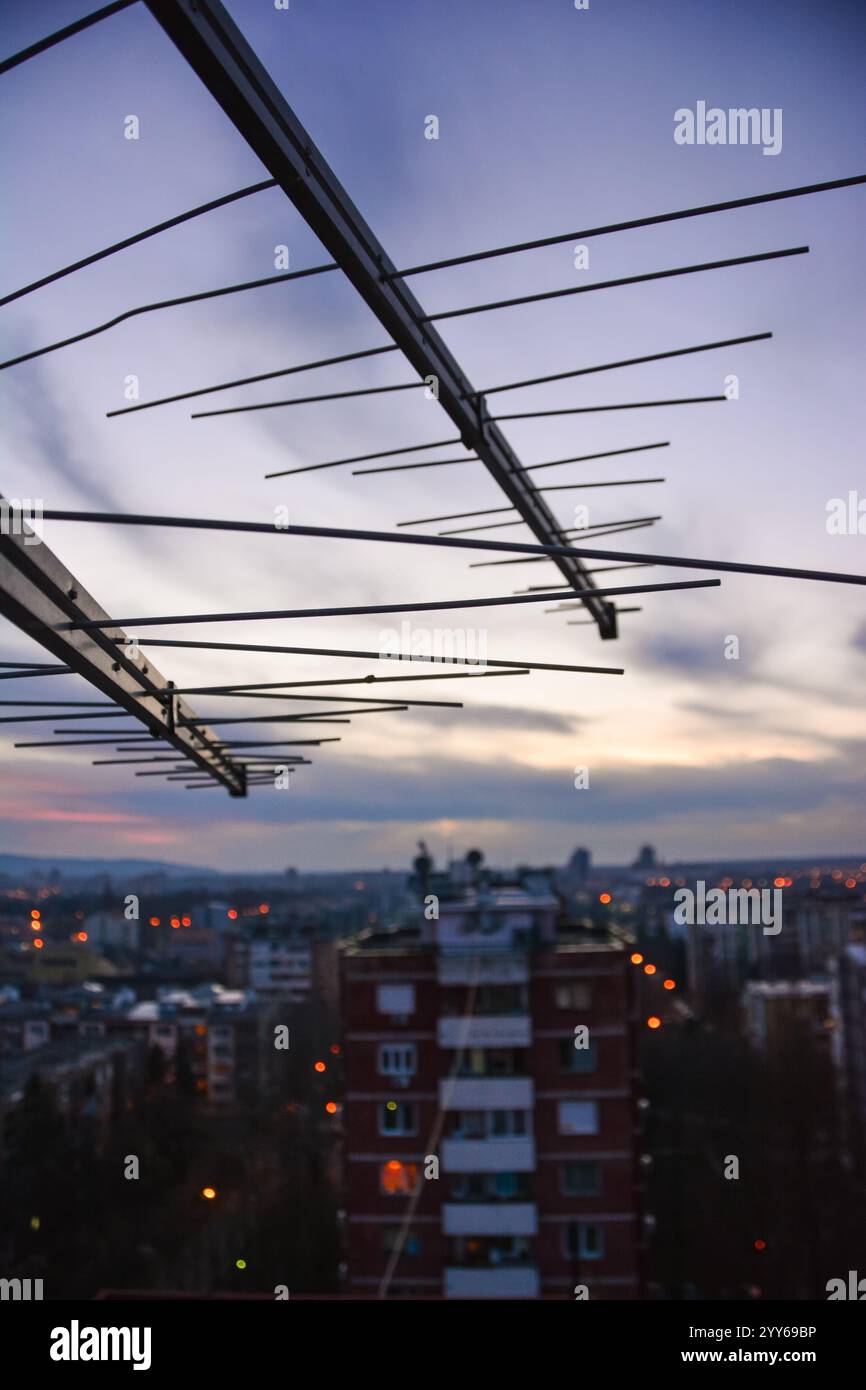 Gros plan de télévision antena sur le toit du bâtiment au coucher du soleil, dans la soirée, avec une belle vue sur la ville en arrière-plan. Banque D'Images