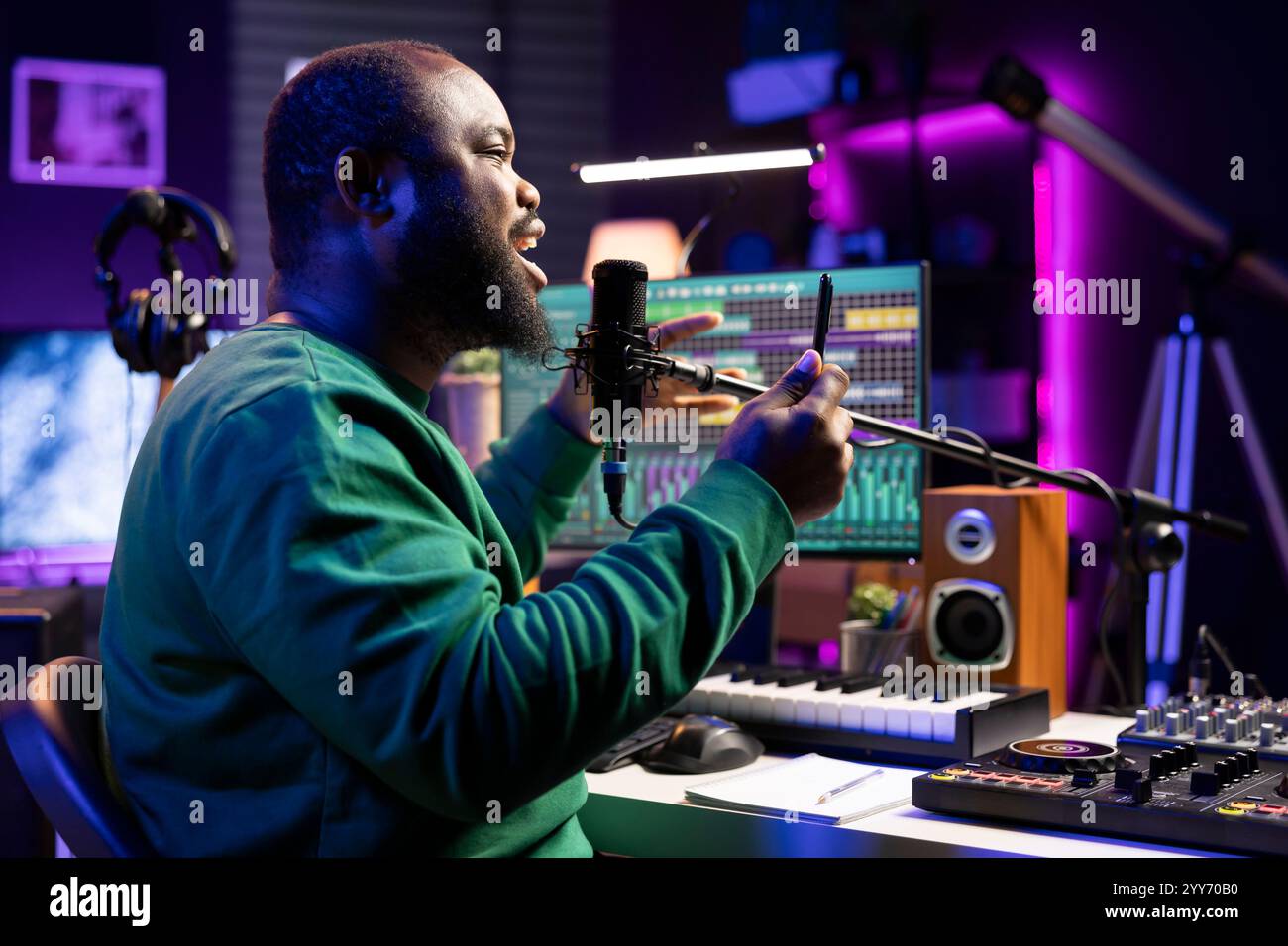 Compositeur afro-américain enregistrant des fichiers audio sur sa chanson, ajoutant des effets spéciaux et éditant avec une console de mixage pour améliorer la qualité sonore. Auteur-compositeur artiste masculin se produisant au microphone. Banque D'Images