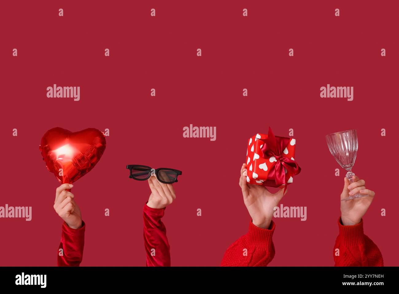 Mains féminines avec lunettes 3D, boîte-cadeau, verre à vin et ballon à air en forme de coeur sur fond rouge. Célébration de la Saint-Valentin Banque D'Images