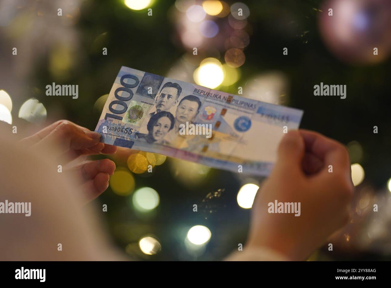Chine. 20 décembre 2024. Dans cette illustration, une personne tient des billets de banque en peso philippin avec des lumières de Noël en arrière-plan. Crédit : SOPA images Limited/Alamy Live News Banque D'Images