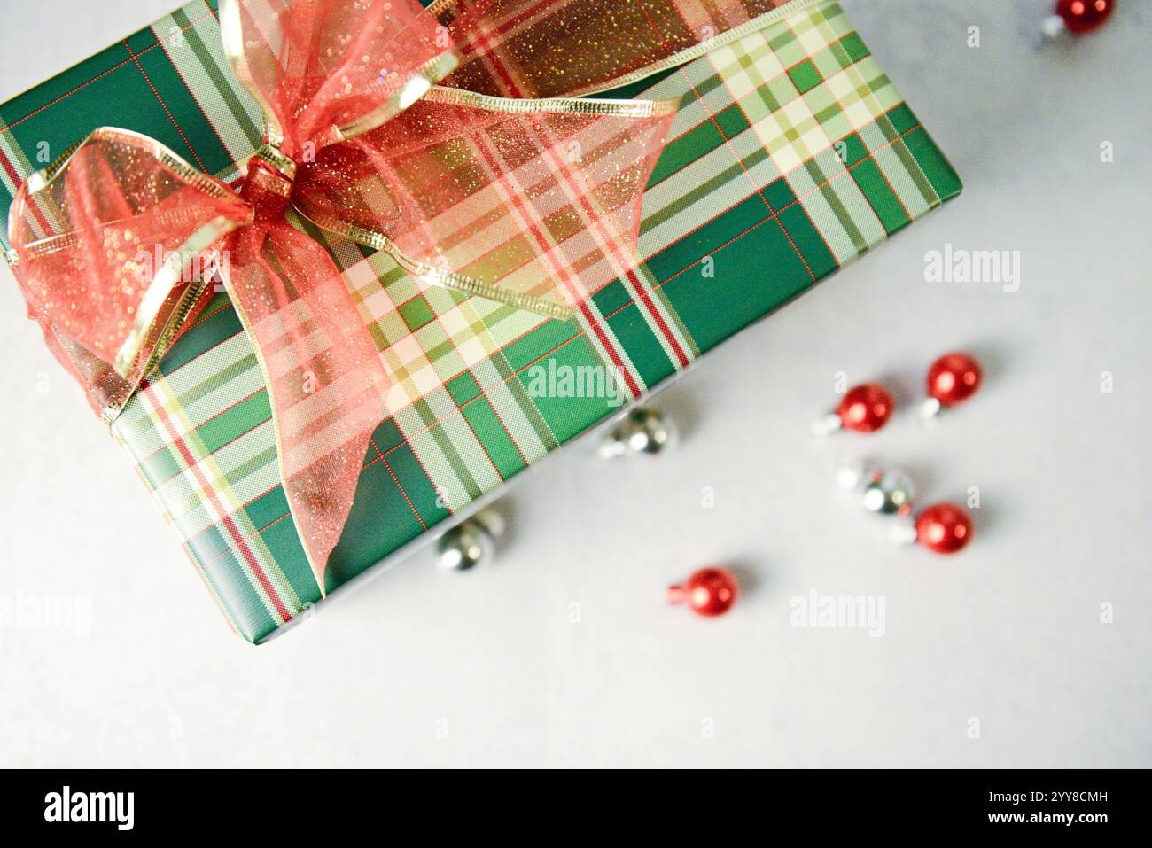 Cadeau à carreaux avec noeud rouge pailleté entouré d'ornements brillants. Banque D'Images