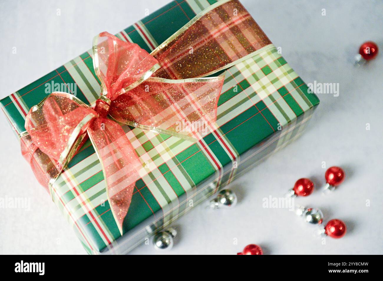 Cadeau festif à carreaux avec noeud rouge scintillant entouré d'ornements Banque D'Images