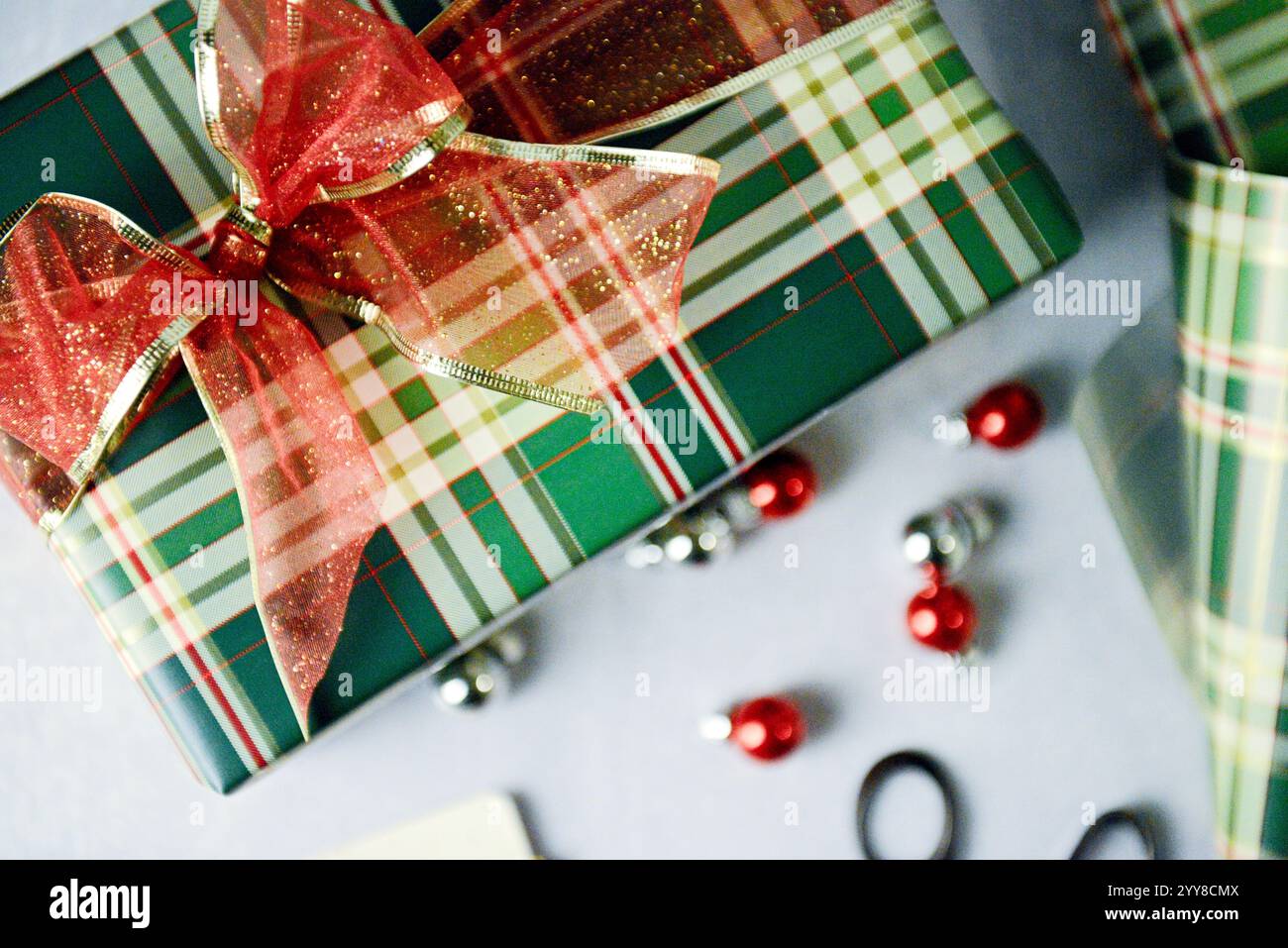 Cadeau enveloppé de carreaux avec noeud rouge pailleté et ornements festifs Banque D'Images