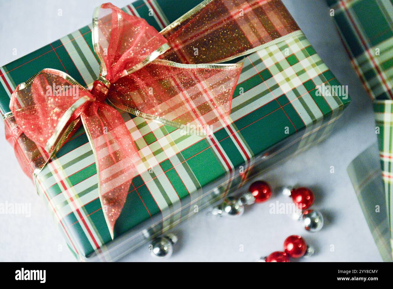 Cadeau enveloppé de carreaux avec noeud rouge pailleté et ornements festifs. Banque D'Images