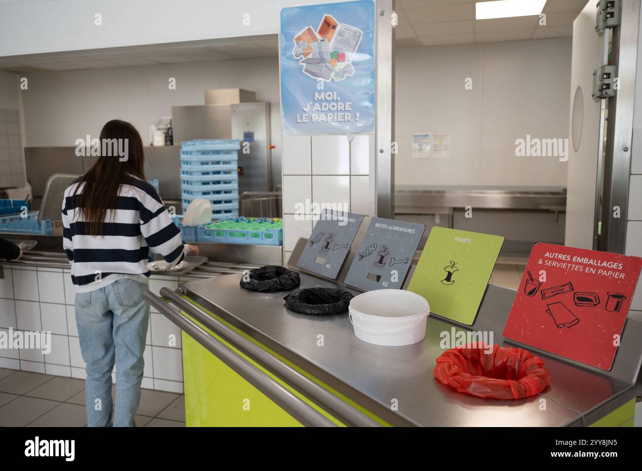 Restauration institutionnelle : une écolière près des poubelles de tri dans une cafétéria scolaire, triant les déchets après avoir terminé le déjeuner. Tri des aliments et non-fo Banque D'Images