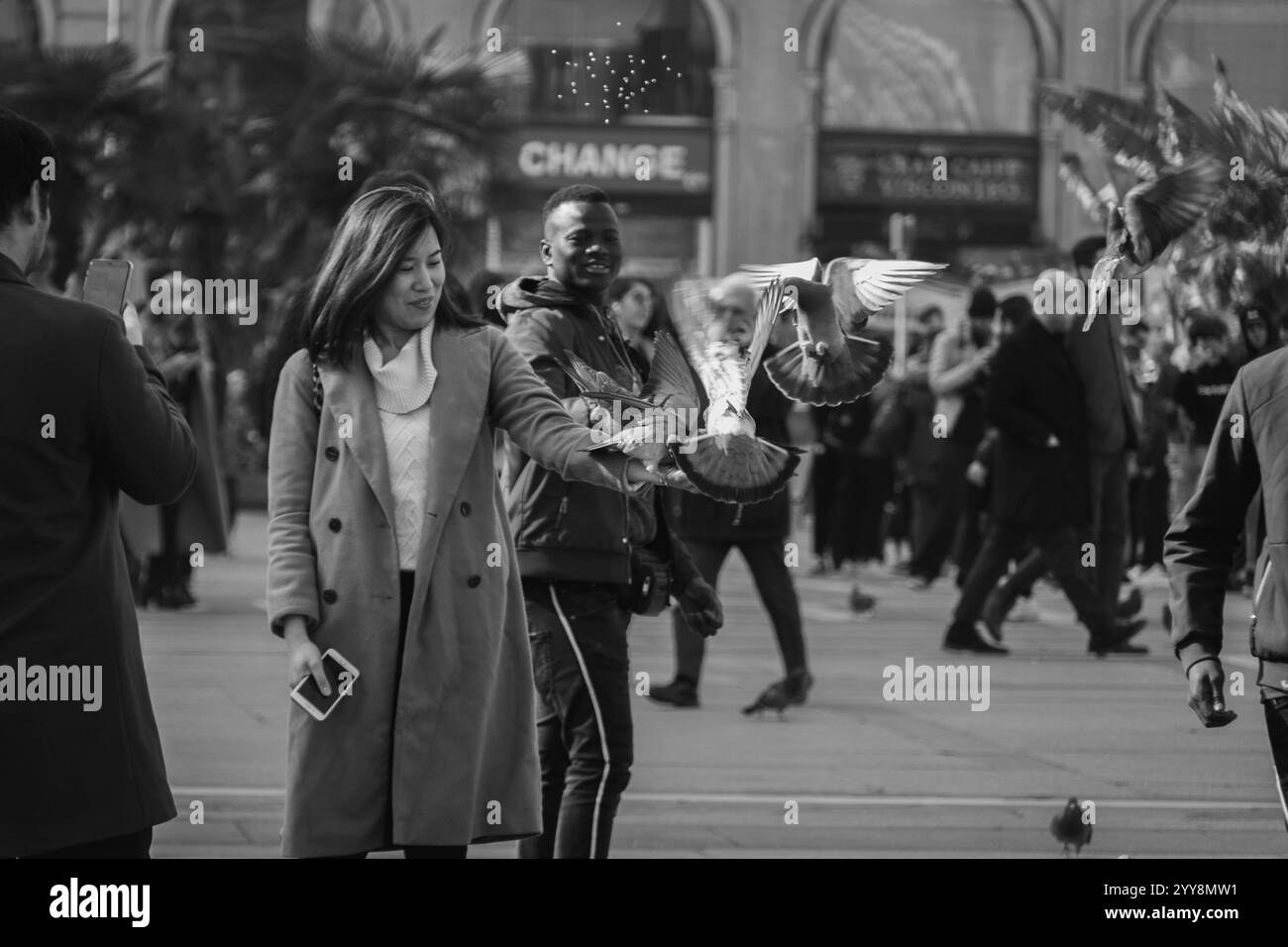 Un moment fugace capturé en noir et blanc, alors qu’une femme nourrit un pigeon en plein vol, symbole d’harmonie et de grâce Banque D'Images