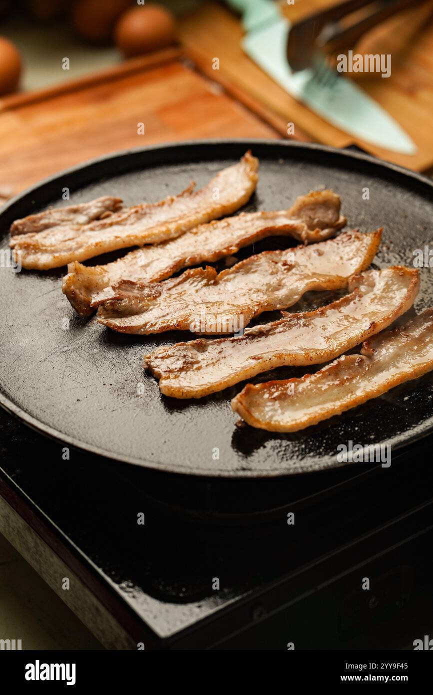 Les tranches de poitrine de porc grésillantes cuisent sur une plaque chauffante : bords croustillants, centre juteux et cette irrésistible gâteau doré en cours. Banque D'Images