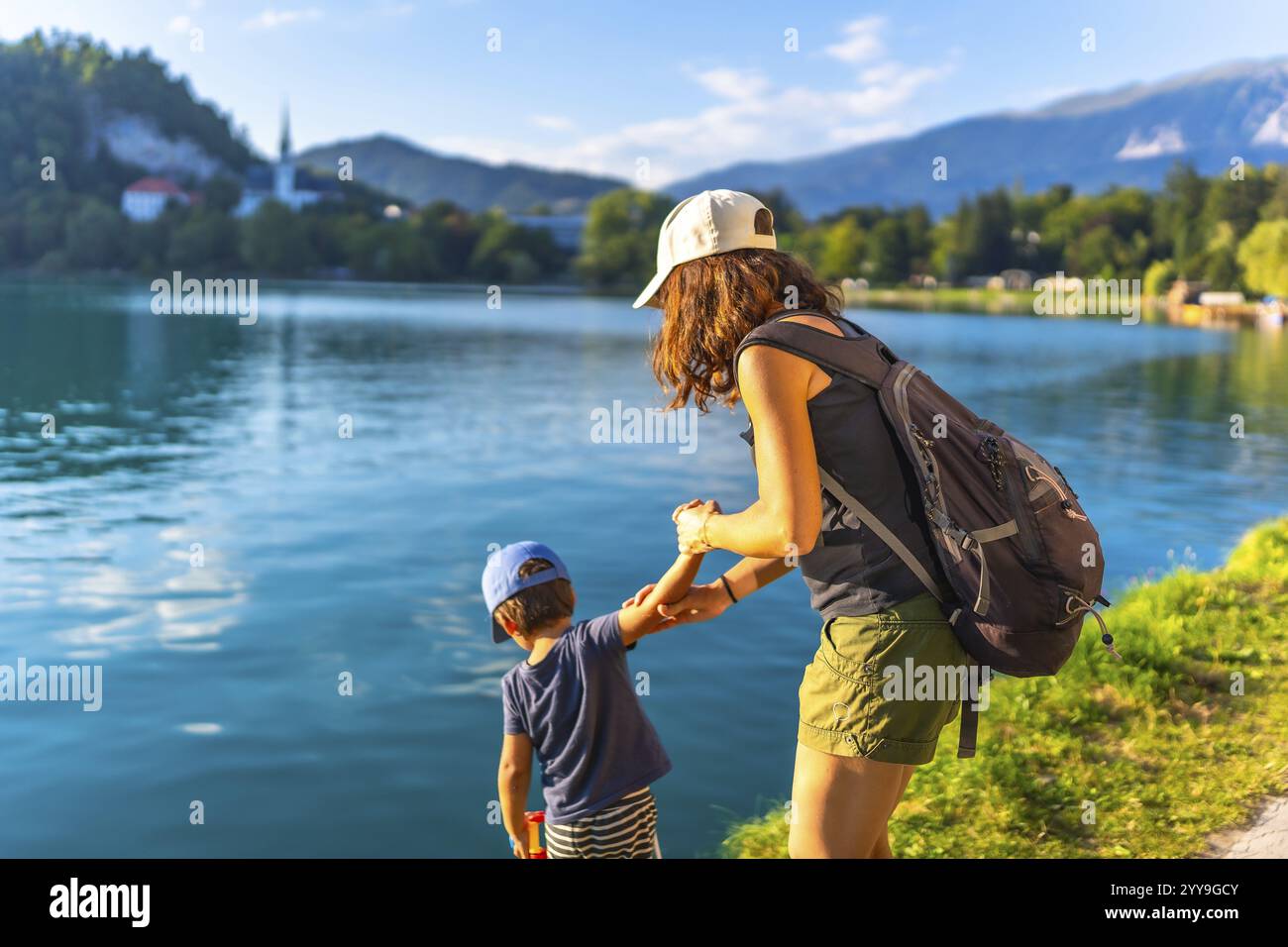 Mère et fils se tenant la main, profitant des vacances d'été au bord de l'eau turquoise du lac saigné, avec l'église emblématique sur l'île saignée en arrière-plan Banque D'Images