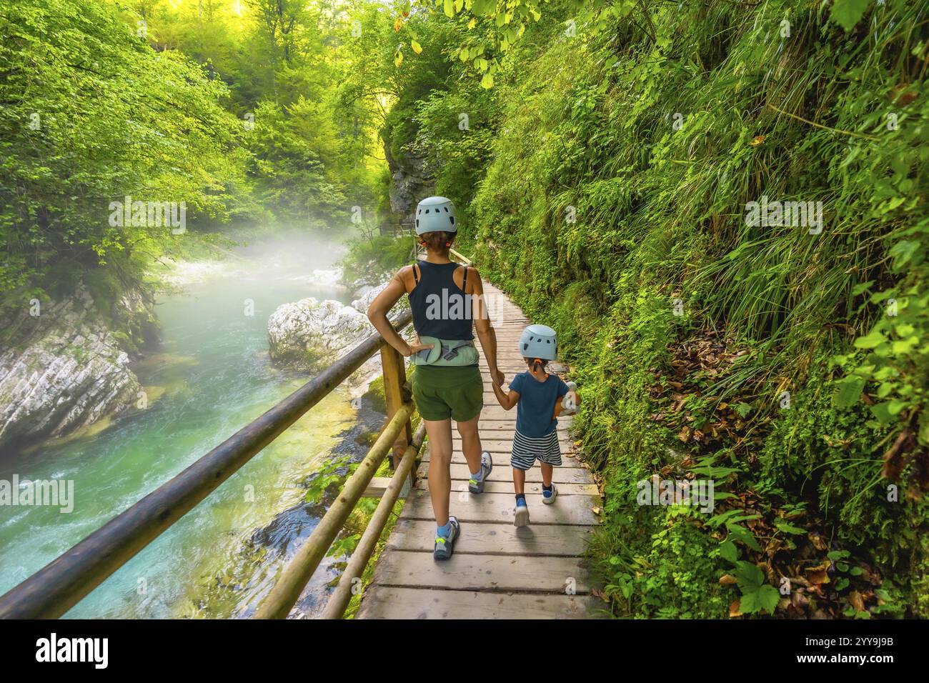 Mère et fils portant des casques marchent sur un sentier en bois le long d'une rivière immaculée, profitant du paysage magnifique de la gorge vintgar près de Bled, s. Banque D'Images