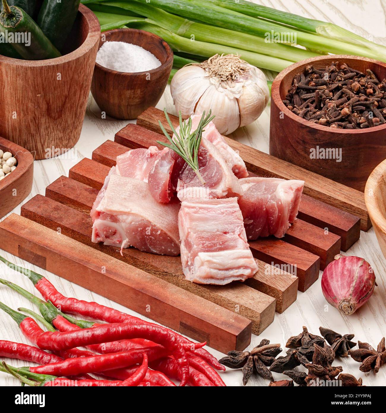 Viande de chèvre fraîche hachée crue sur une planche de bois entourée d'ingrédients de cuisine traditionnels tels que le gingembre, les oignons, l'ail, les piments secs Banque D'Images