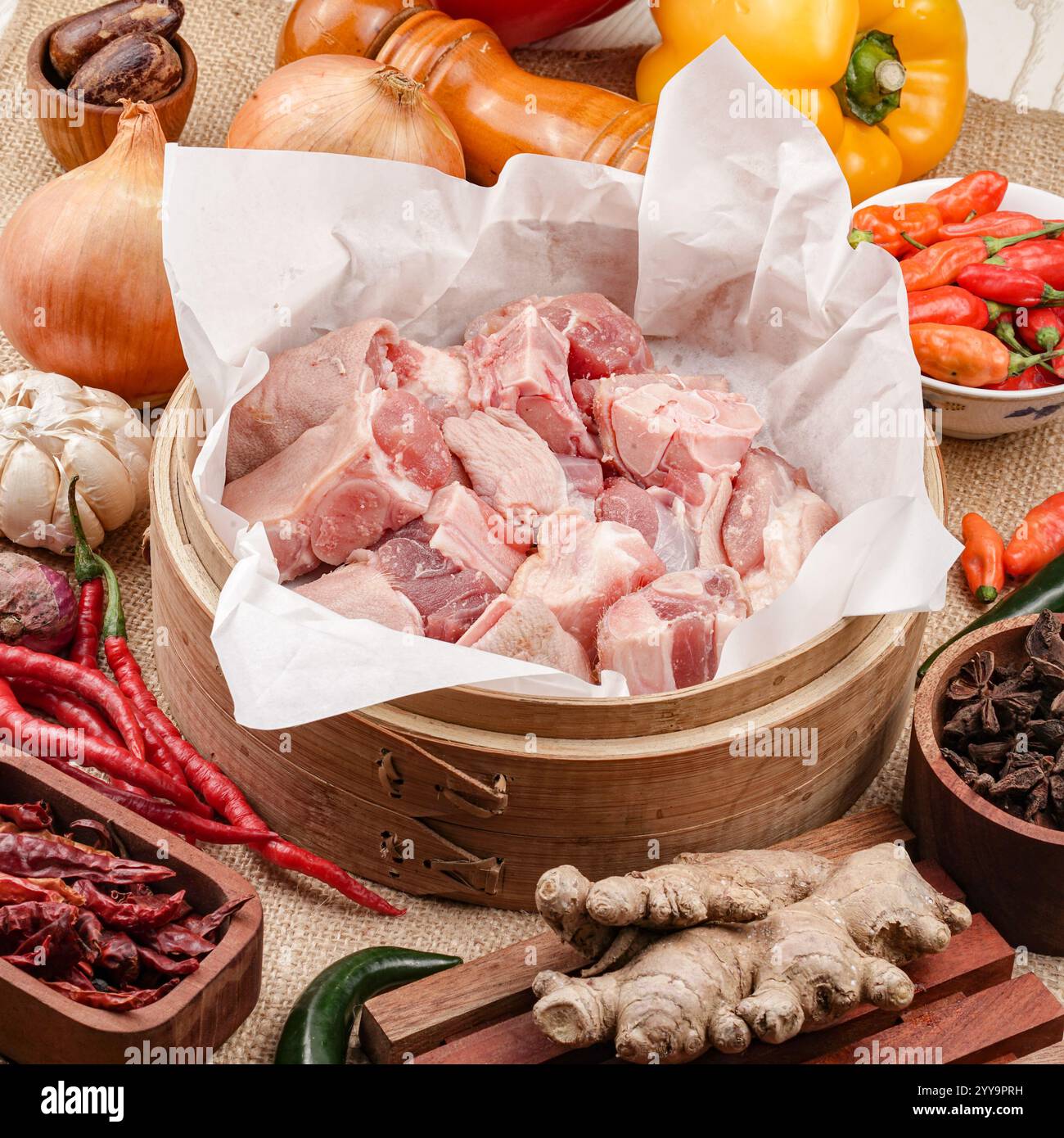 Viande de chèvre fraîche hachée crue sur une planche de bois entourée d'ingrédients de cuisine traditionnels tels que le gingembre, les oignons, l'ail, les piments secs Banque D'Images