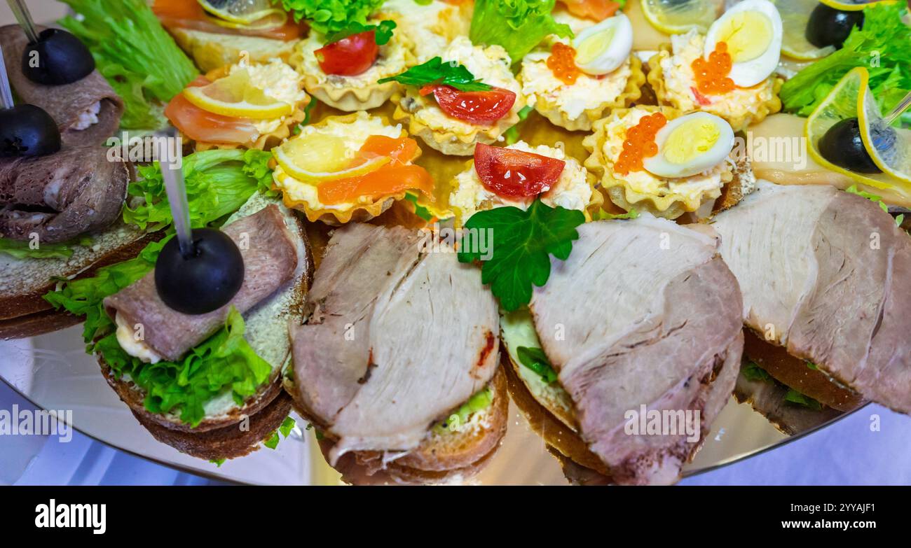 Un plateau festif présente une variété de sandwichs gastronomiques et d'élégants hors-d'œuvre, magnifiquement agencés avec des garnitures et des garnitures fraîches, parfait Banque D'Images