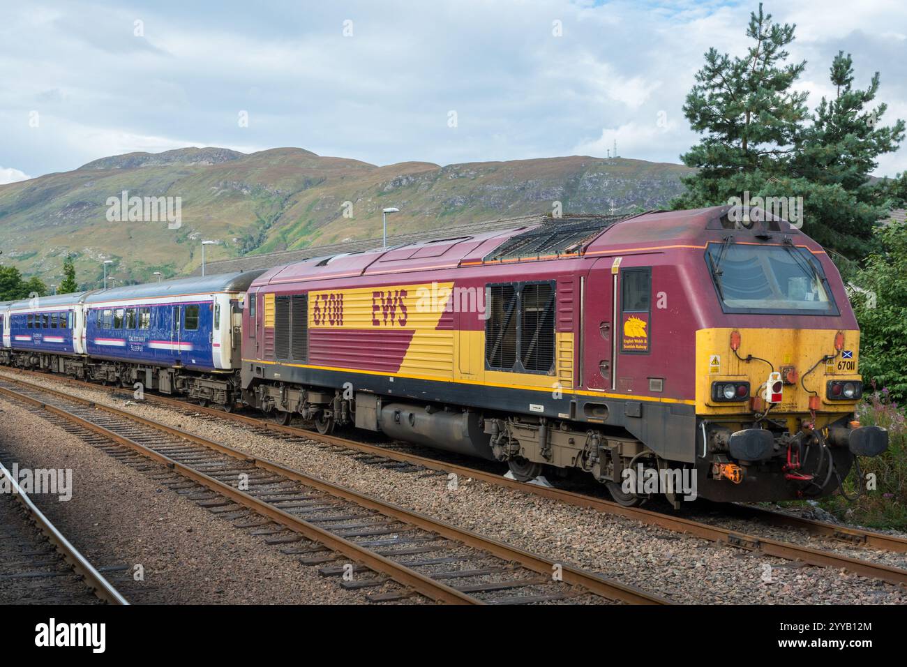 Une locomotive diesel de classe 67 en livrée EWS transportant le train Caledonian Sleeper à la gare de Fort William, avec des montagnes en arrière-plan Banque D'Images