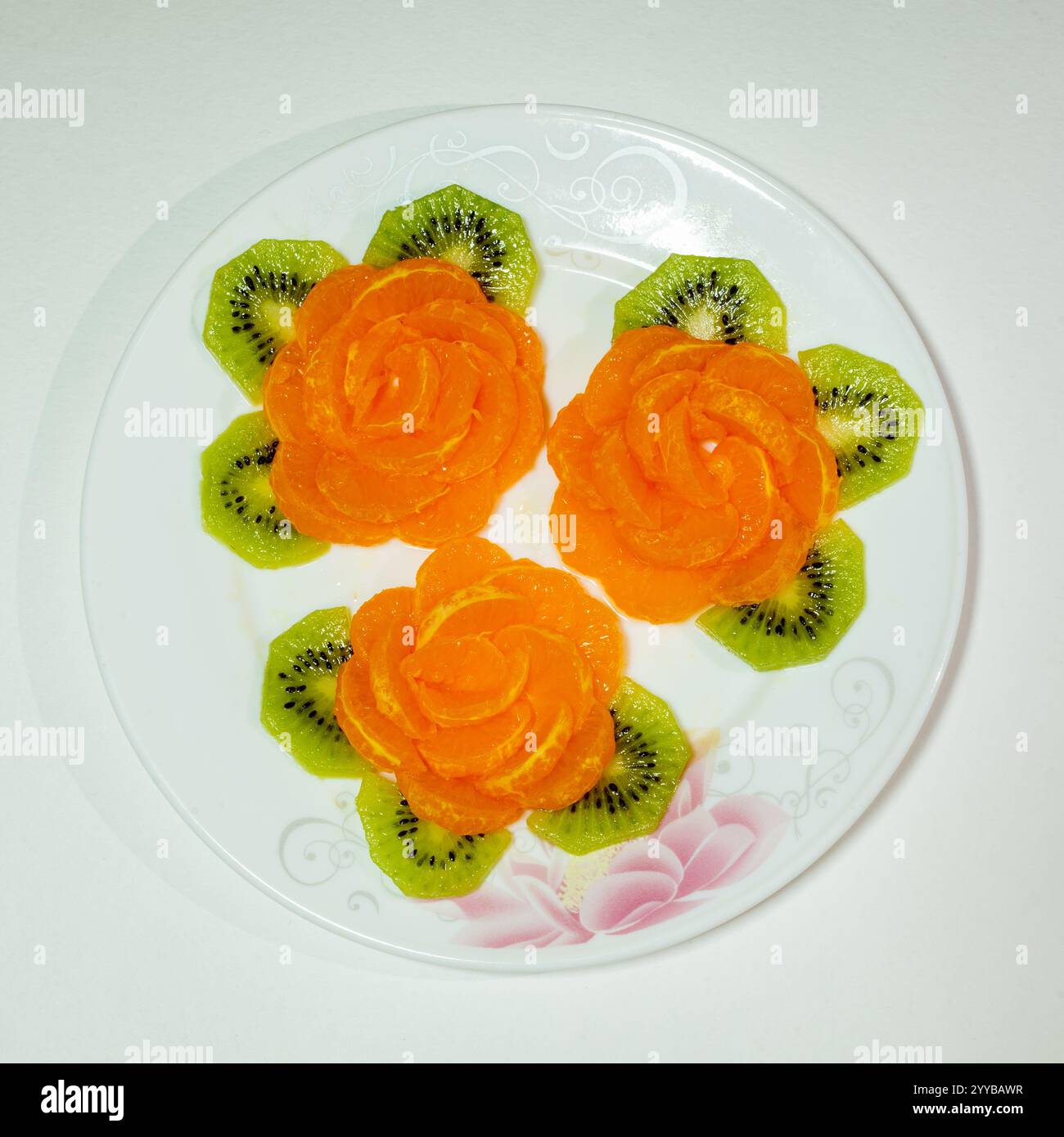 Une vitrine de fruits vibrante avec des tranches d'orange façonnées en forme de rose, entourées de kiwis verts. Cette présentation artistique est parfaite pour une fraîcheur Banque D'Images