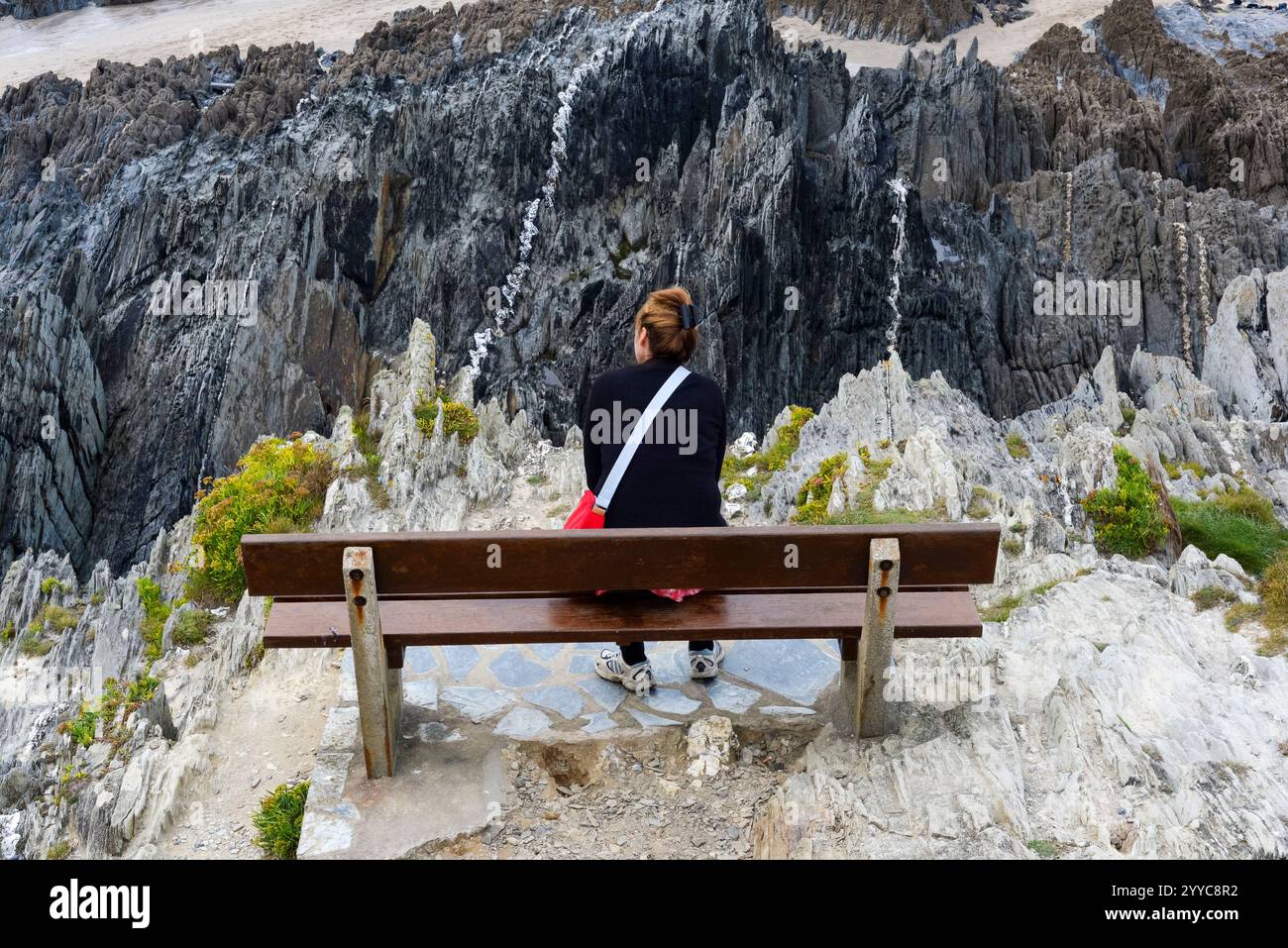 Femme assise sur un banc au sommet de falaises déchiquetées Banque D'Images