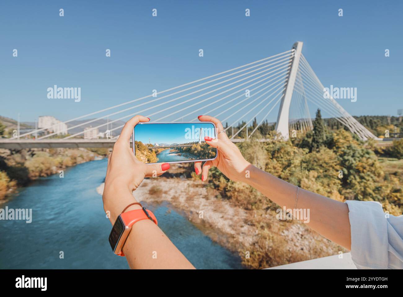 Une jeune femme tenant son smartphone sur un pont à Podgorica, Monténégro, capturant une image du magnifique paysage. Banque D'Images