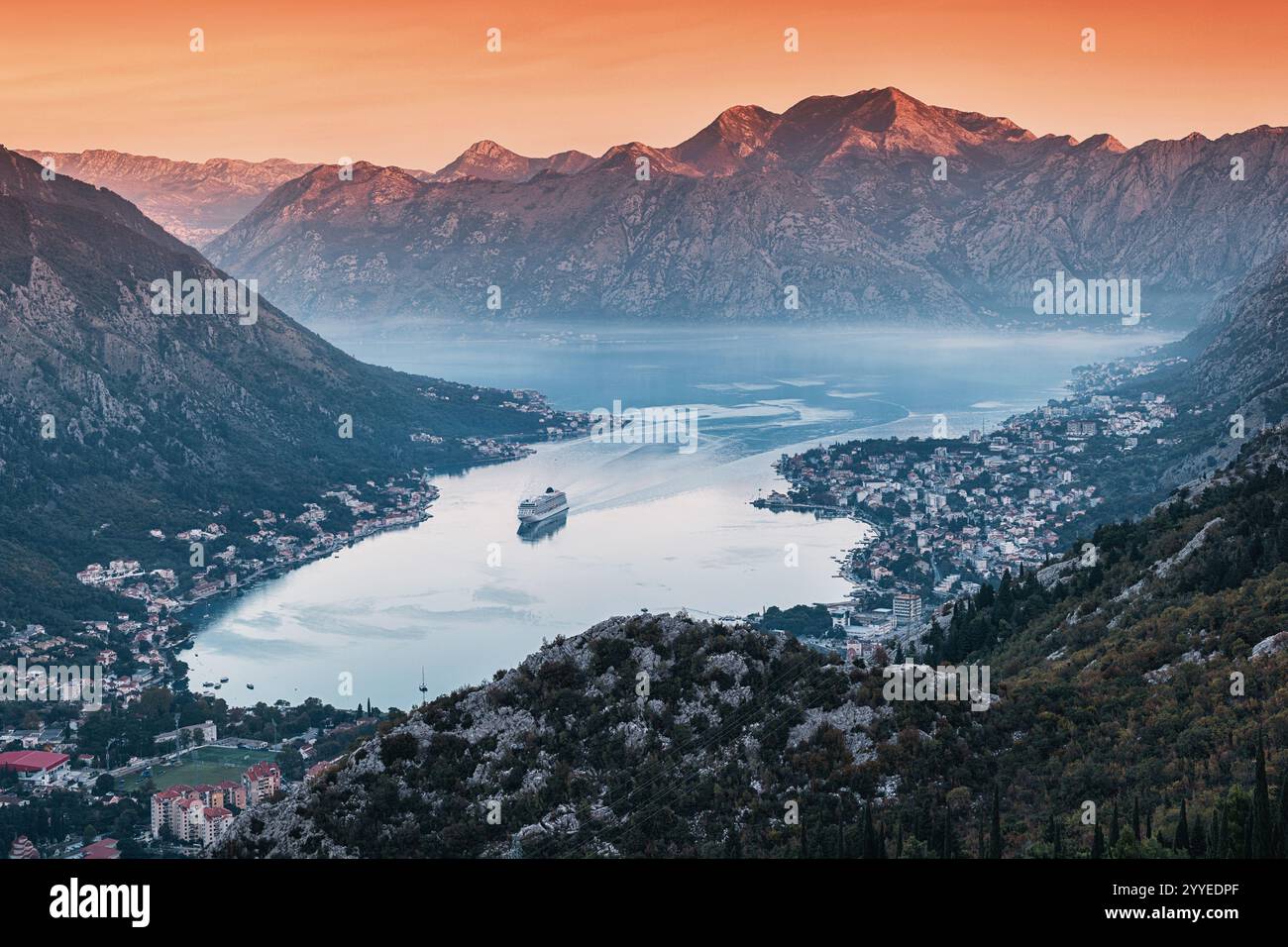 Vue aérienne à couper le souffle de la baie de Kotor avec bateau de croisière naviguant dans des eaux calmes lors d'un coucher de soleil vibrant, entouré de montagnes majestueuses, Monténégro Banque D'Images