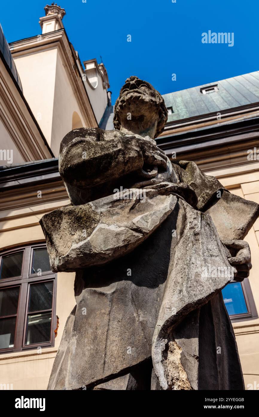 Une statue d'un homme se dresse devant un bâtiment. La statue est faite de pierre et a un chapeau de pierre sur sa tête. Le bâtiment est grand et a un toit bleu Banque D'Images