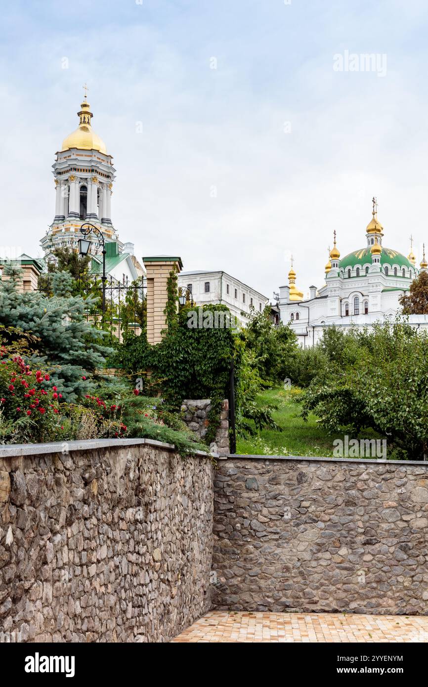 Un mur de pierre avec une haie verte et un bâtiment avec un dôme doré. Le bâtiment est une église Banque D'Images