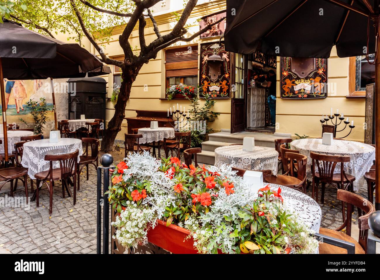 Un patio de restaurant avec tables et chaises, et une grande plante en pot avec des fleurs rouges au milieu Banque D'Images