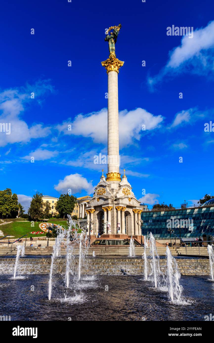 Une grande colonne blanche avec une statue d'une femme sur le dessus. La colonne est entourée d'une fontaine dont l'eau jaillit. Le ciel est bleu et il y a un Banque D'Images