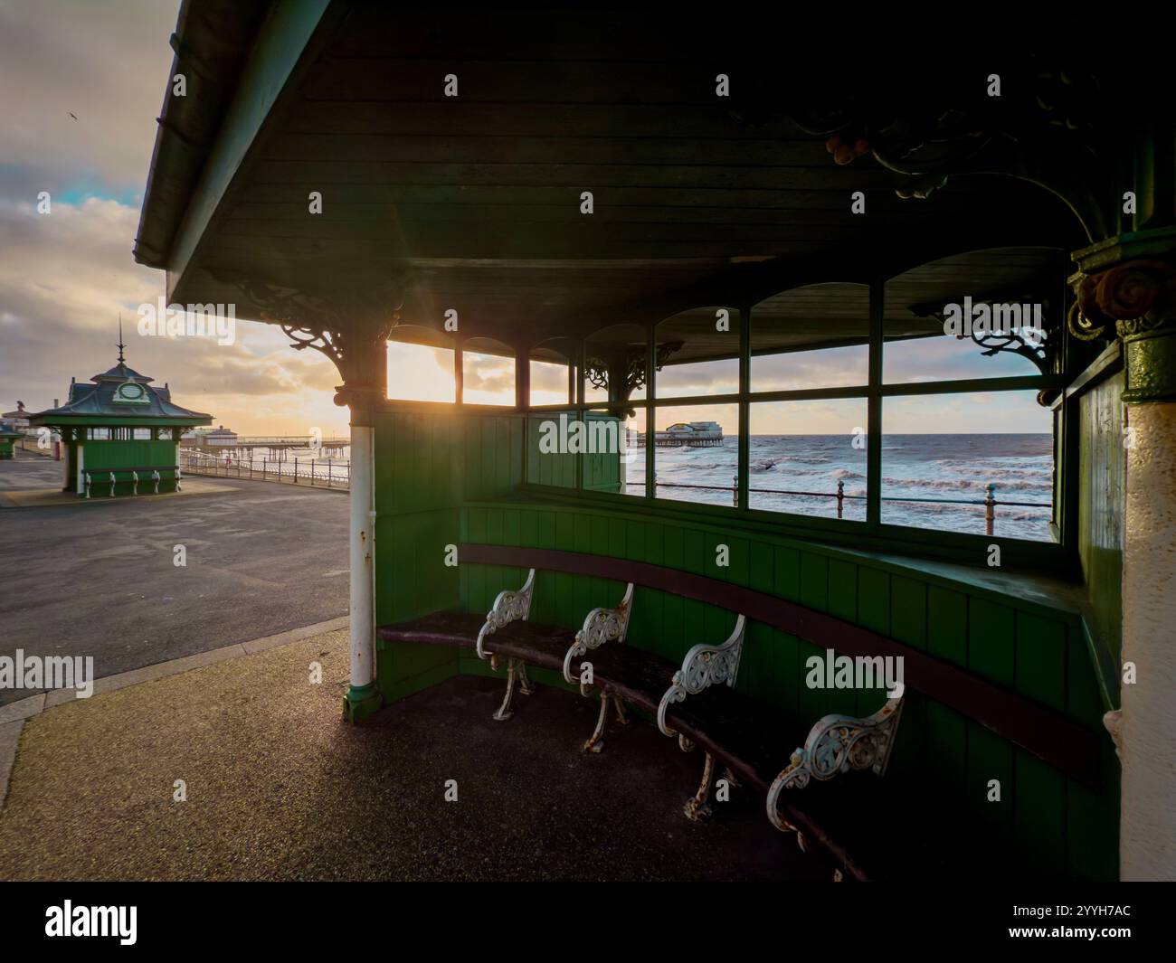 Abris traditionnels en bois vert sur North Promenade à Blackpool avec coucher de soleil derrière North Pier au loin. - Image de stock capturée avec un smartphone