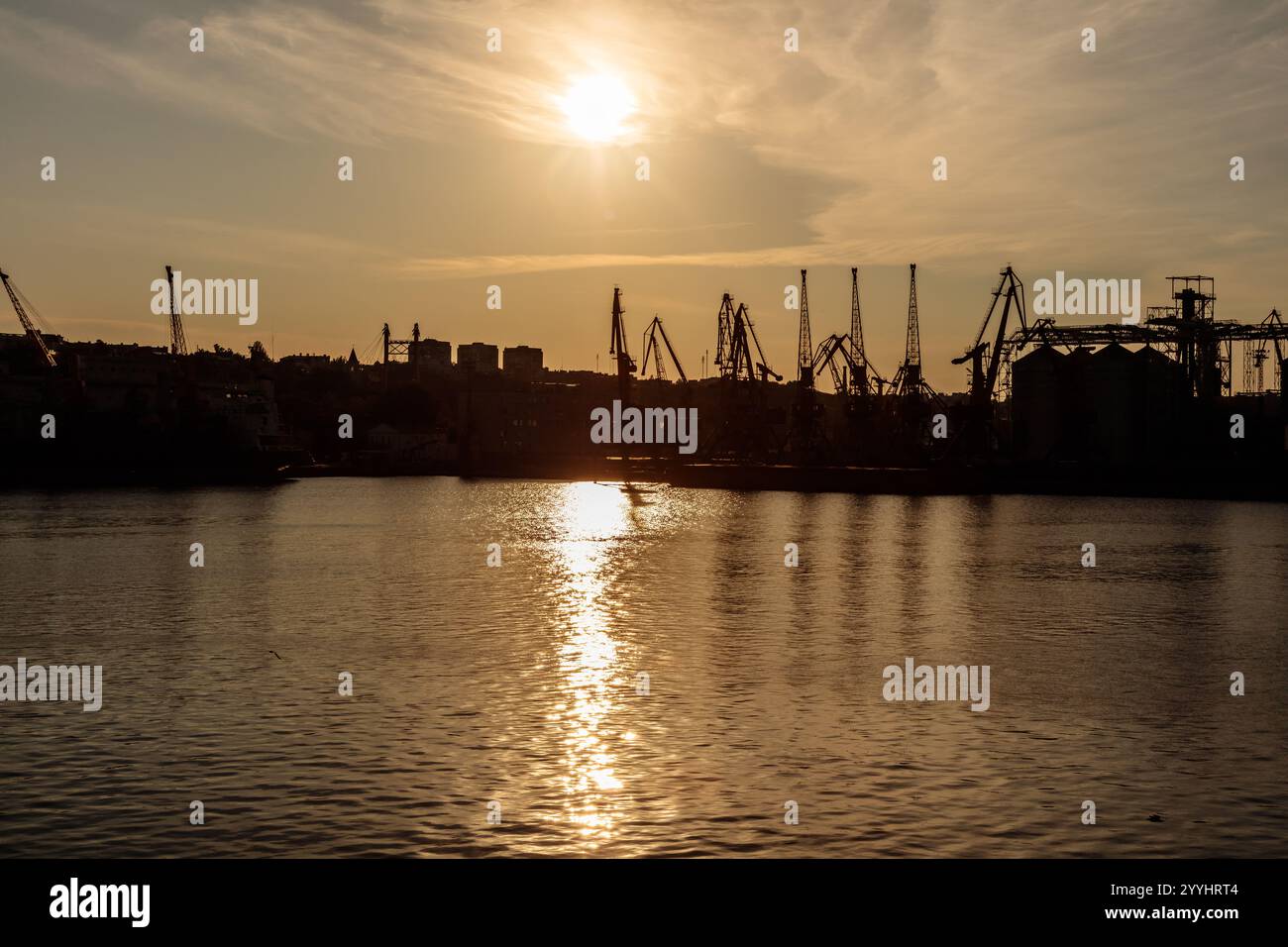 L'image capture un beau coucher de soleil sur un plan d'eau calme, avec une grande grue visible en arrière-plan. La scène est paisible et sereine, avec Banque D'Images