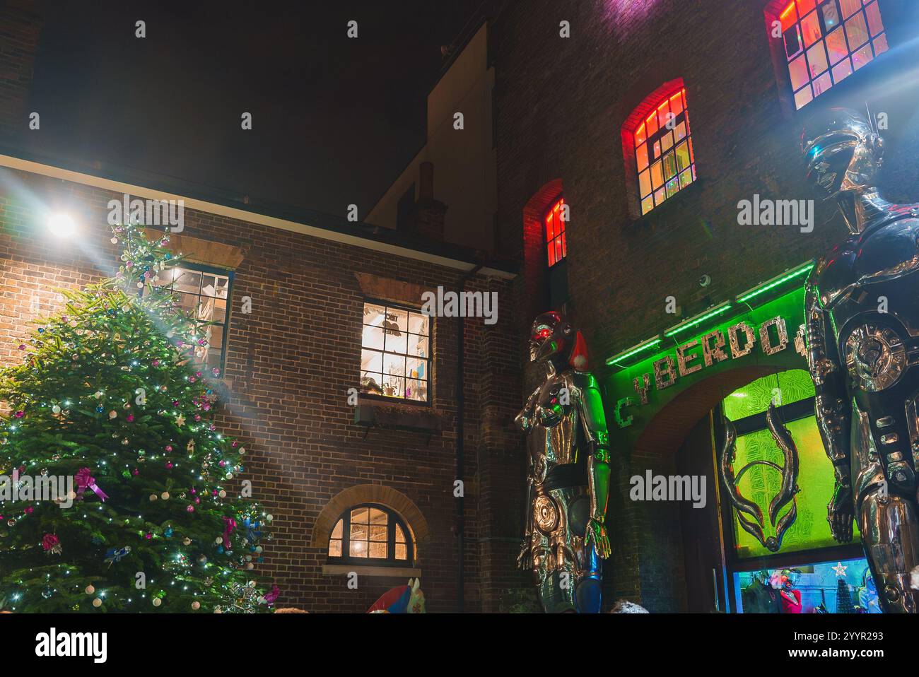 Un grand sapin de Noël décoré se dresse devant le magasin Cyberdog à Camden Market, Londres. Des enseignes vert fluo et des figures métalliques soulignent l'orl Banque D'Images