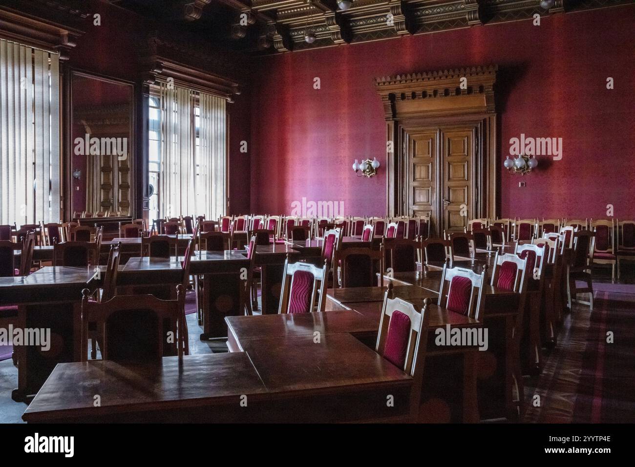 Une grande salle avec de nombreuses chaises et tables en bois. La chambre est rouge et a une atmosphère très formelle Banque D'Images