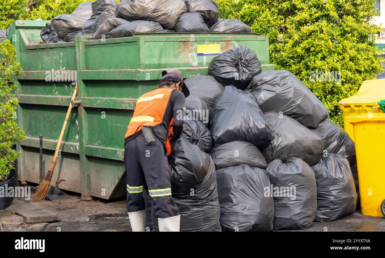 Le travailleur des ordures ou le collecteur de déchets travaille et collecte les ordures dans des sacs en plastique noirs dans la pile géante en ville. Banque D'Images