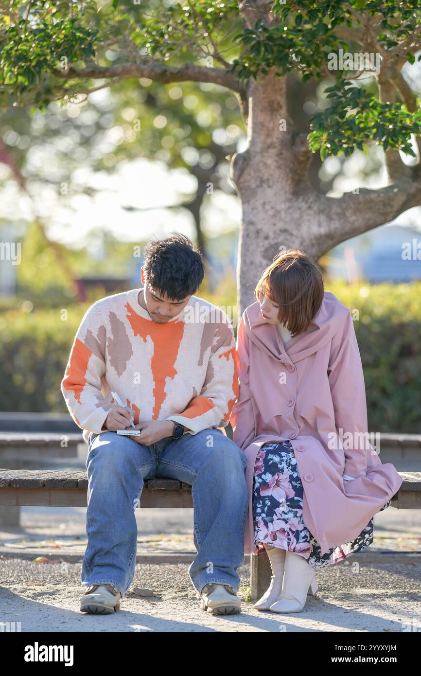 Un couple dans la vingtaine est assis sur un banc et parle dans un grand parc à Handa City, préfecture d'Aichi en automne. Banque D'Images