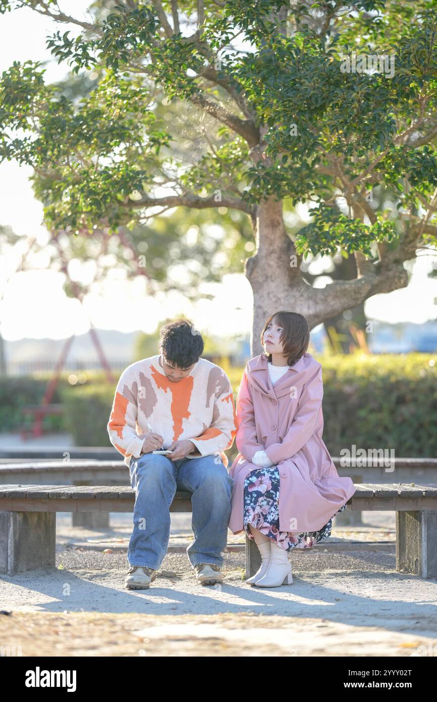 Un couple dans la vingtaine est assis sur un banc et parle dans un grand parc à Handa City, préfecture d'Aichi en automne. Banque D'Images