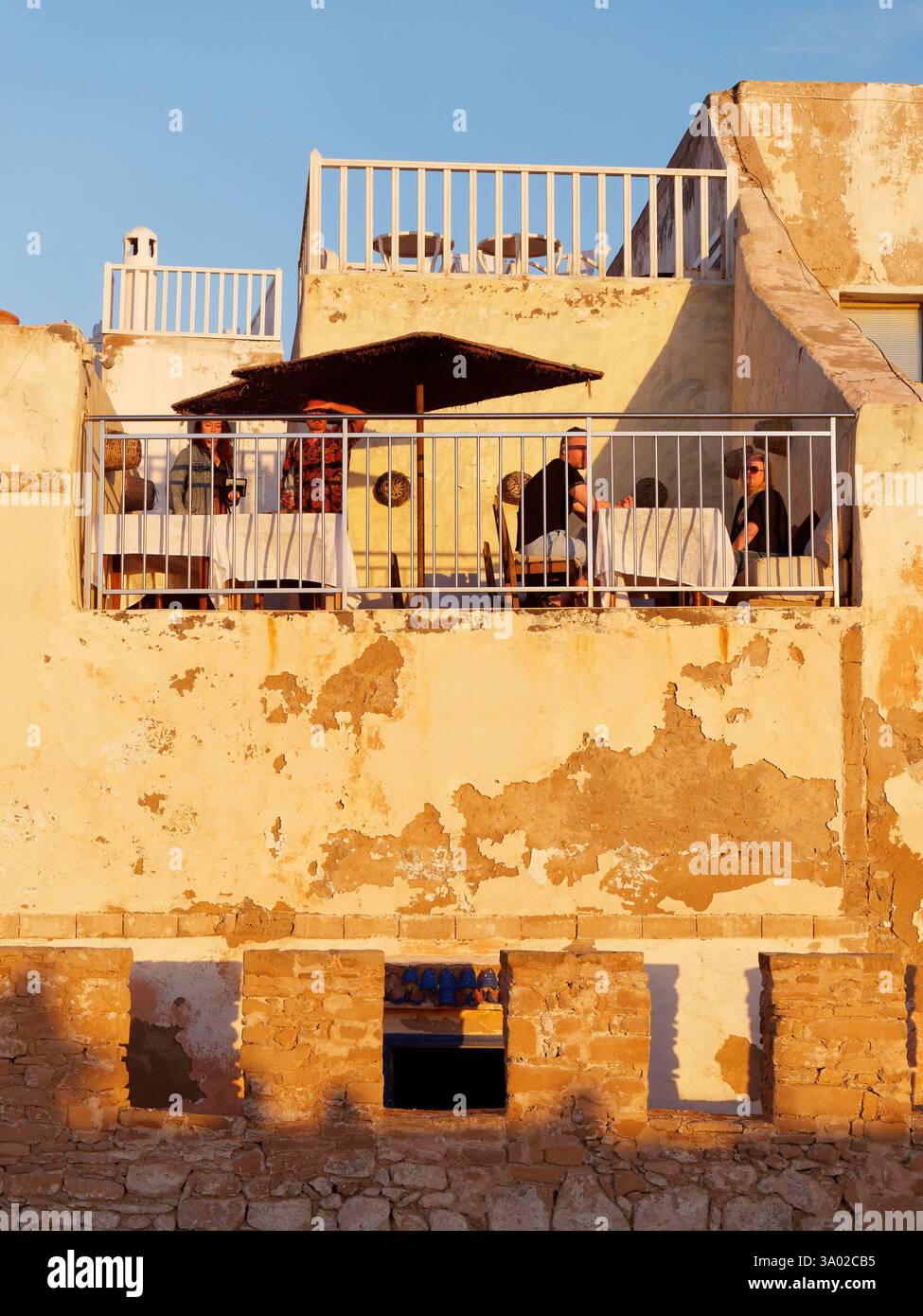 Les gens dans un petit restaurant rustique de base avec des rampes construites dans les murs de la ville un soir dans la médina à Essaouria, Maroc. Février/mars 2025 Banque D'Images