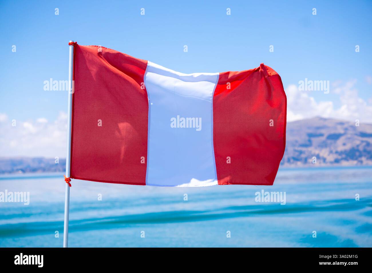 Drapeau du Pérou flottant sur les rives du lac Titicaca, symbolisant la fierté nationale et la culture andine Banque D'Images