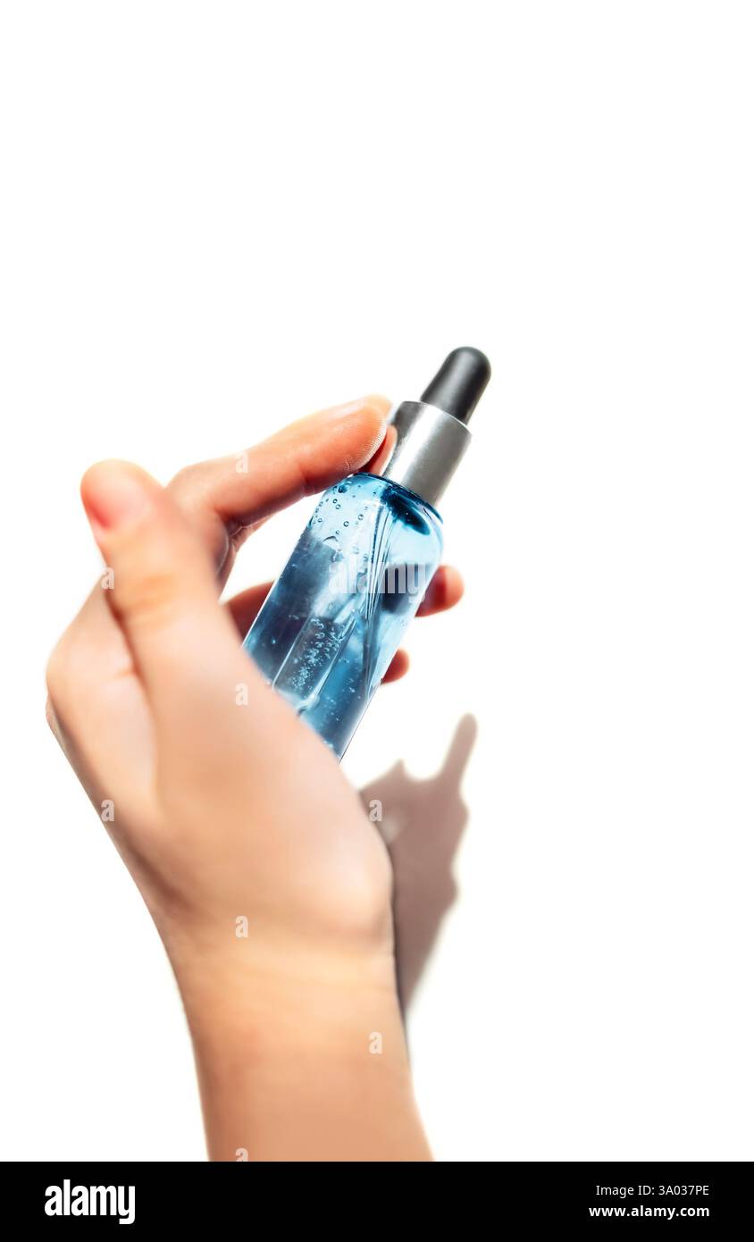 Gros plan d'une main féminine avec une bouteille transparente de sérum hydratant bleu pour le visage. Une jeune femme tient un produit cosmétique. Vitamine anti-agine Banque D'Images