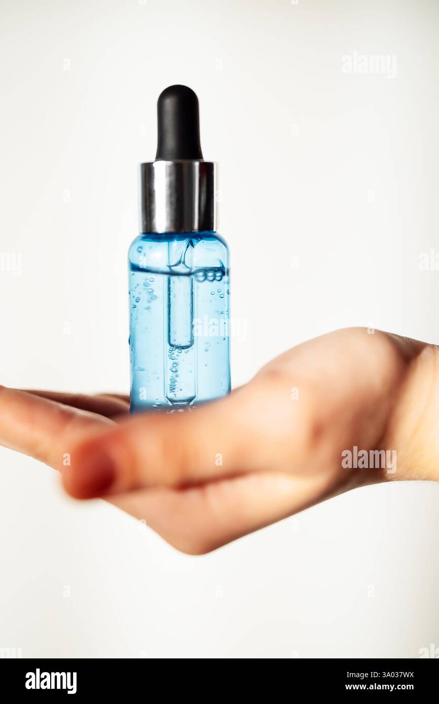 Gros plan d'une main féminine avec une bouteille transparente de sérum hydratant bleu pour le visage. Une jeune femme tient un produit cosmétique. Vitamine anti-agine Banque D'Images