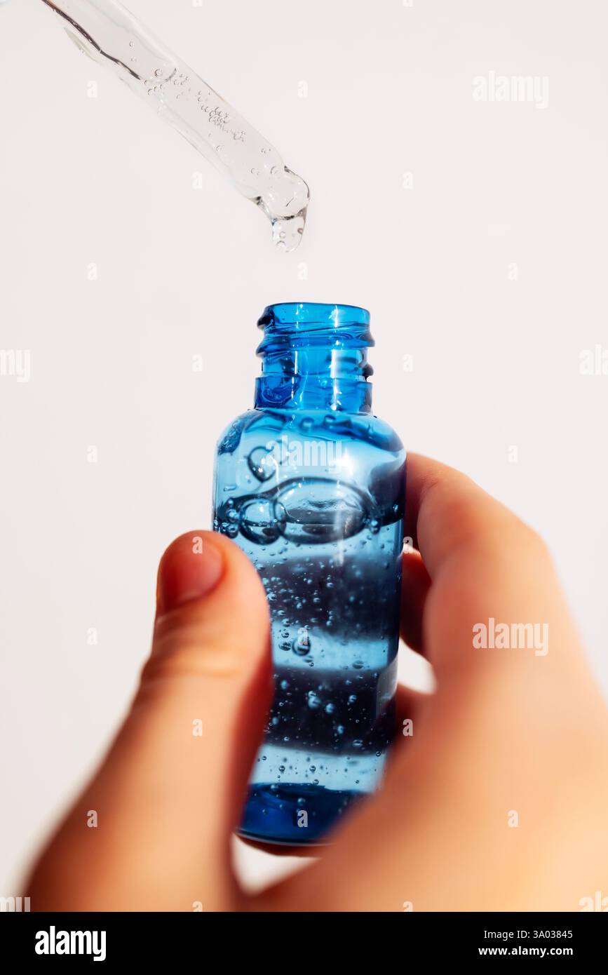 Gros plan d'une main féminine avec une bouteille transparente de sérum hydratant bleu pour le visage. Une jeune femme tient un produit cosmétique. Vitamine anti-agine Banque D'Images