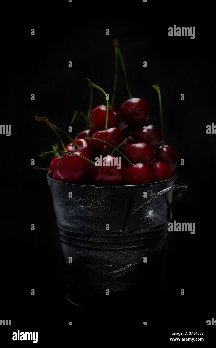 Cerises rouges fraîches dans un seau en métal noir sur un fond sombre Banque D'Images