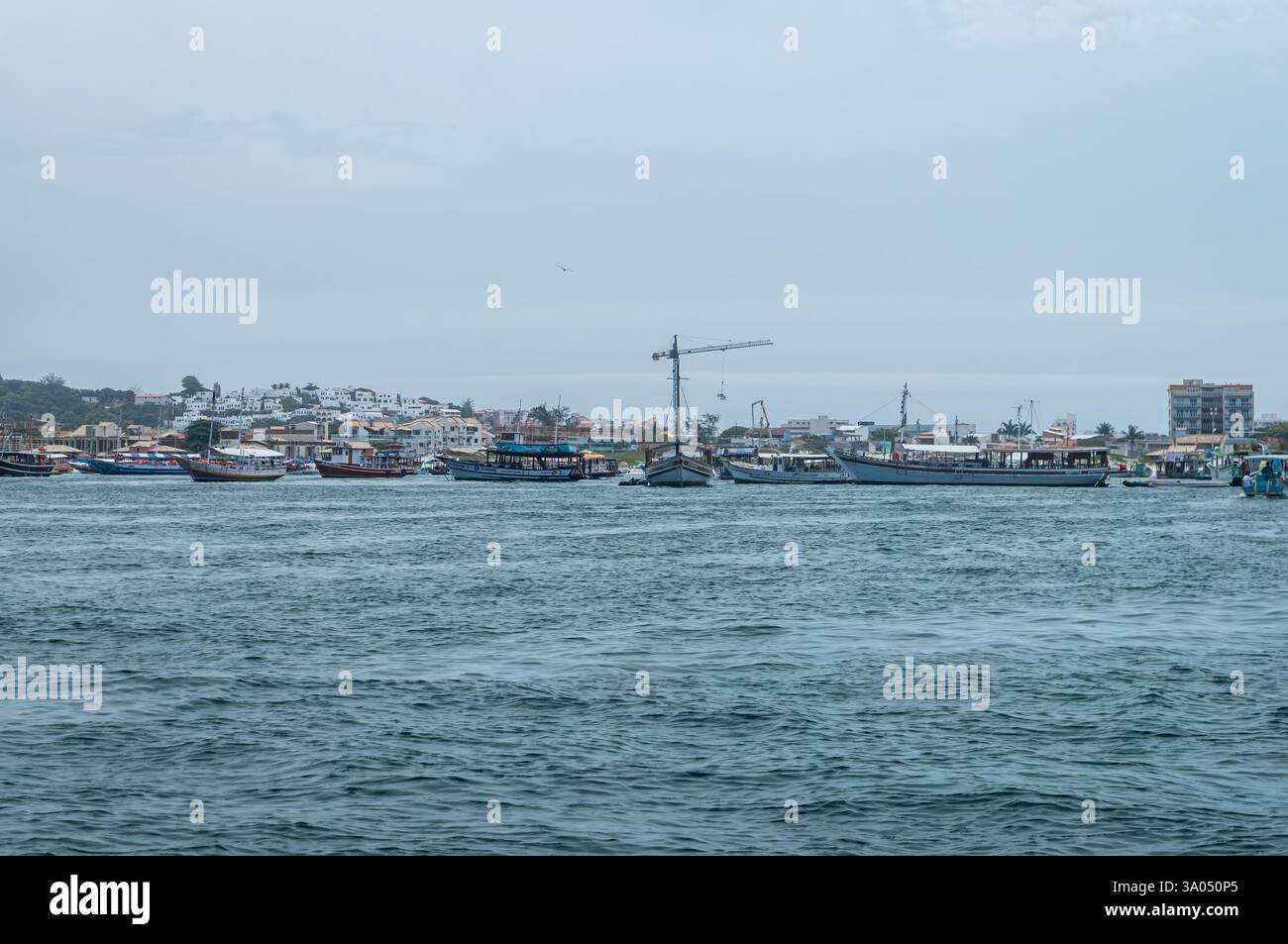 Vue lointaine de la plage de Praia dos Anjos avec des bateaux ancrés et des bâtiments près du port d'Arraial do Cabo sous un ciel ensoleillé chaud en fin d'après-midi. Banque D'Images Vue lointaine de la plage de Praia dos Anjos avec des bateaux ancrés et des bâtiments près du port d'Arraial do Cabo sous un ciel ensoleillé chaud en fin d'après-midi. Banque D'Images