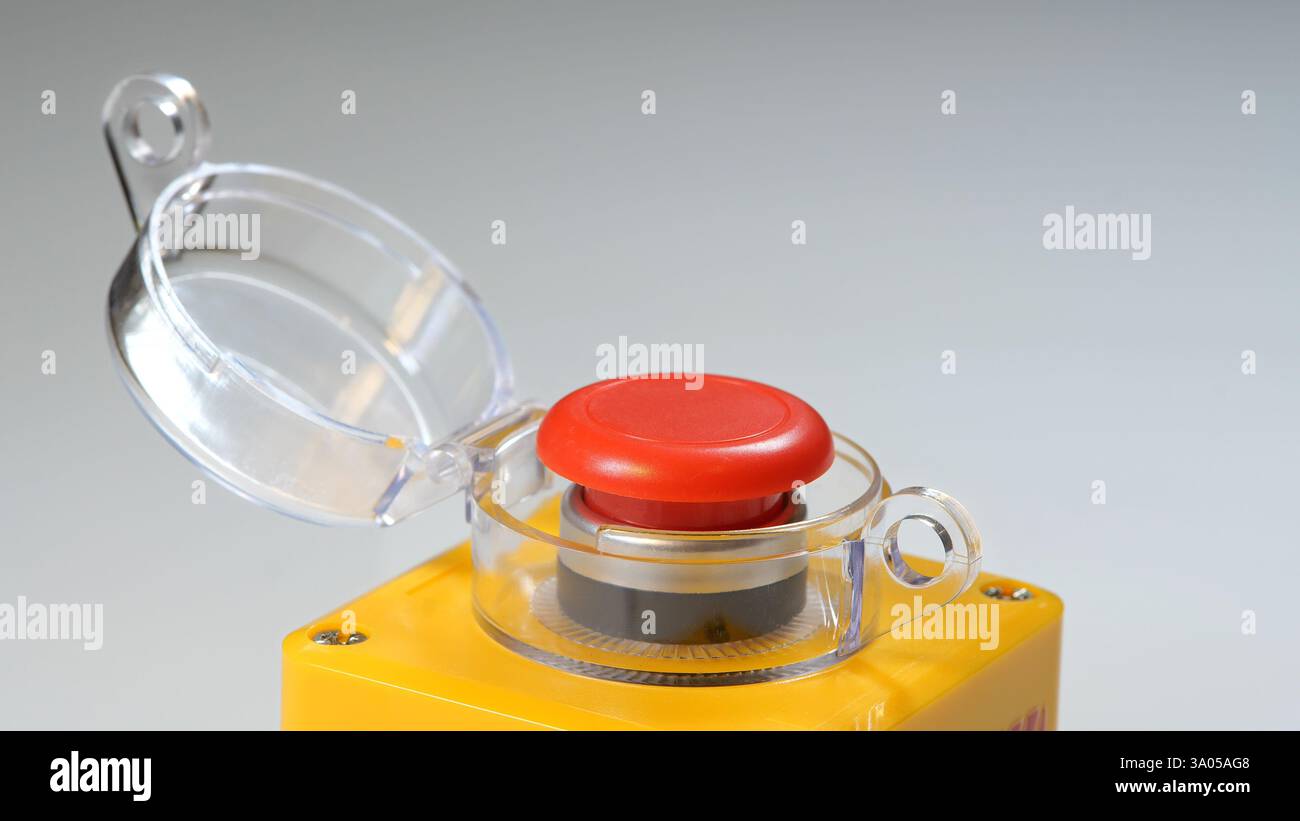 Bouton d'arrêt d'urgence industriel rouge avec couvercle de sécurité transparent ouvert, monté sur le boîtier de commande jaune pour l'arrêt de la machine, interrupteur de sécurité pour l'usine Banque D'Images