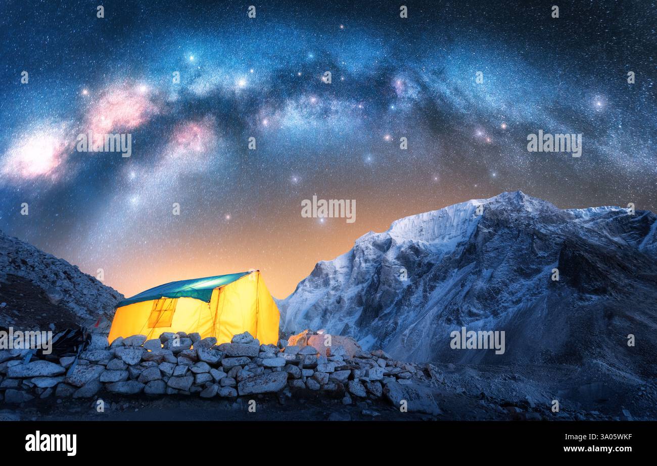 Voie lactée, tente jaune incandescente dans les montagnes enneigées à la nuit étoilée Banque D'Images