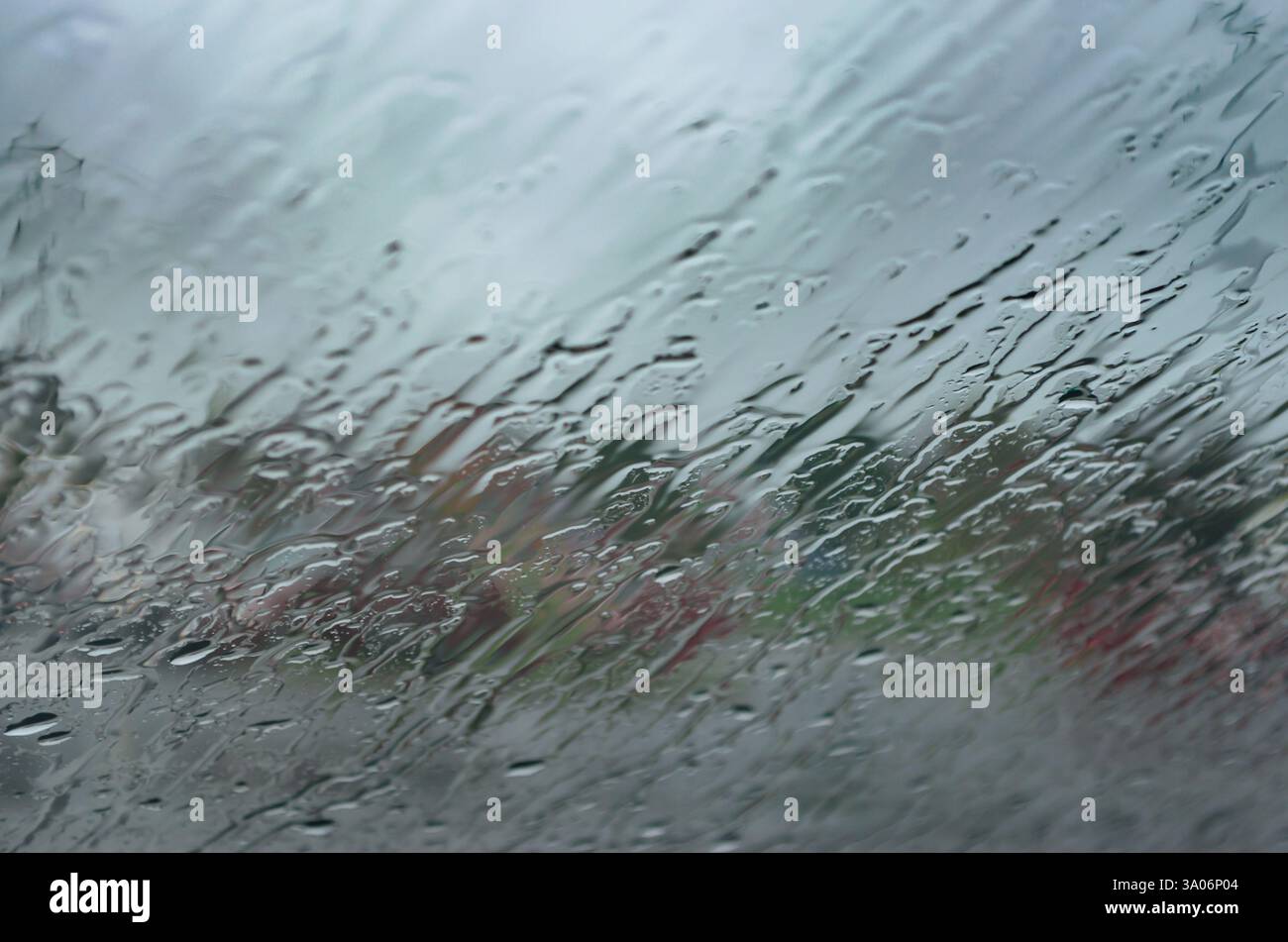 Vue abstraite avec des gouttes de pluie qui coulent en diagonale sur un pare-brise avec des motifs de couleur sourds. Banque D'Images