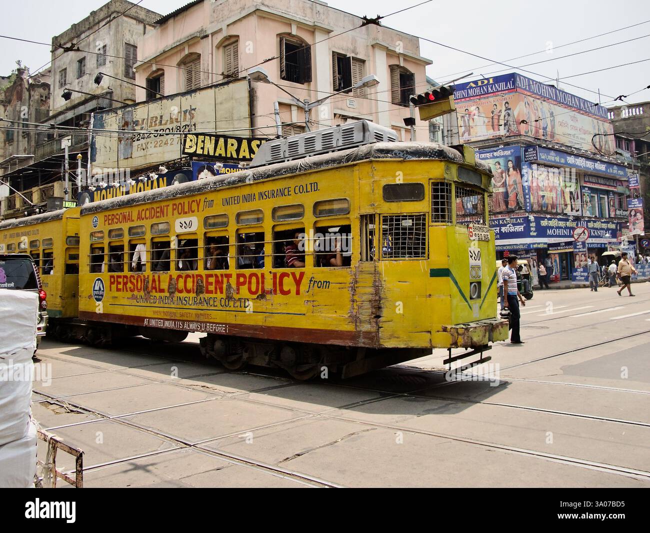Un tramway jaune historique à Kolkata naviguant dans une zone commerciale animée, reflétant le réseau de tramways unique et en déclin de la ville. Banque D'Images