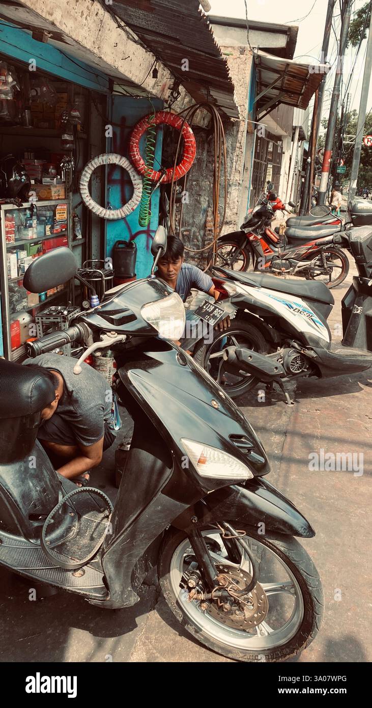 Jakarta, vendredi 7 juillet 2024 - Un mécanicien local en bordure de route travaille sur une moto dans un petit atelier de réparation. Un regard brut et authentique sur la vie quotidienne - Image de stock capturée avec un smartphone