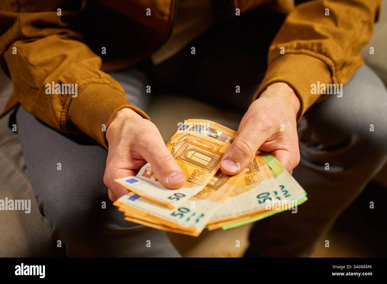 Gros plan d'un homme comptant des billets en euros chez lui. Personne planifiant ses finances personnelles, assis sur un canapé avec de l'argent comptant. Concept de planification du budget de la maison, de l'épargne et des finances personnelles Banque D'Images